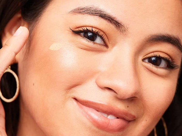 Smiling woman applying cream to her cheekbones