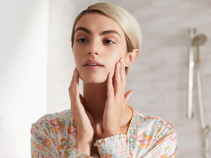 Image of a woman with short blonde hair touching the sides of her face while looking in the mirror